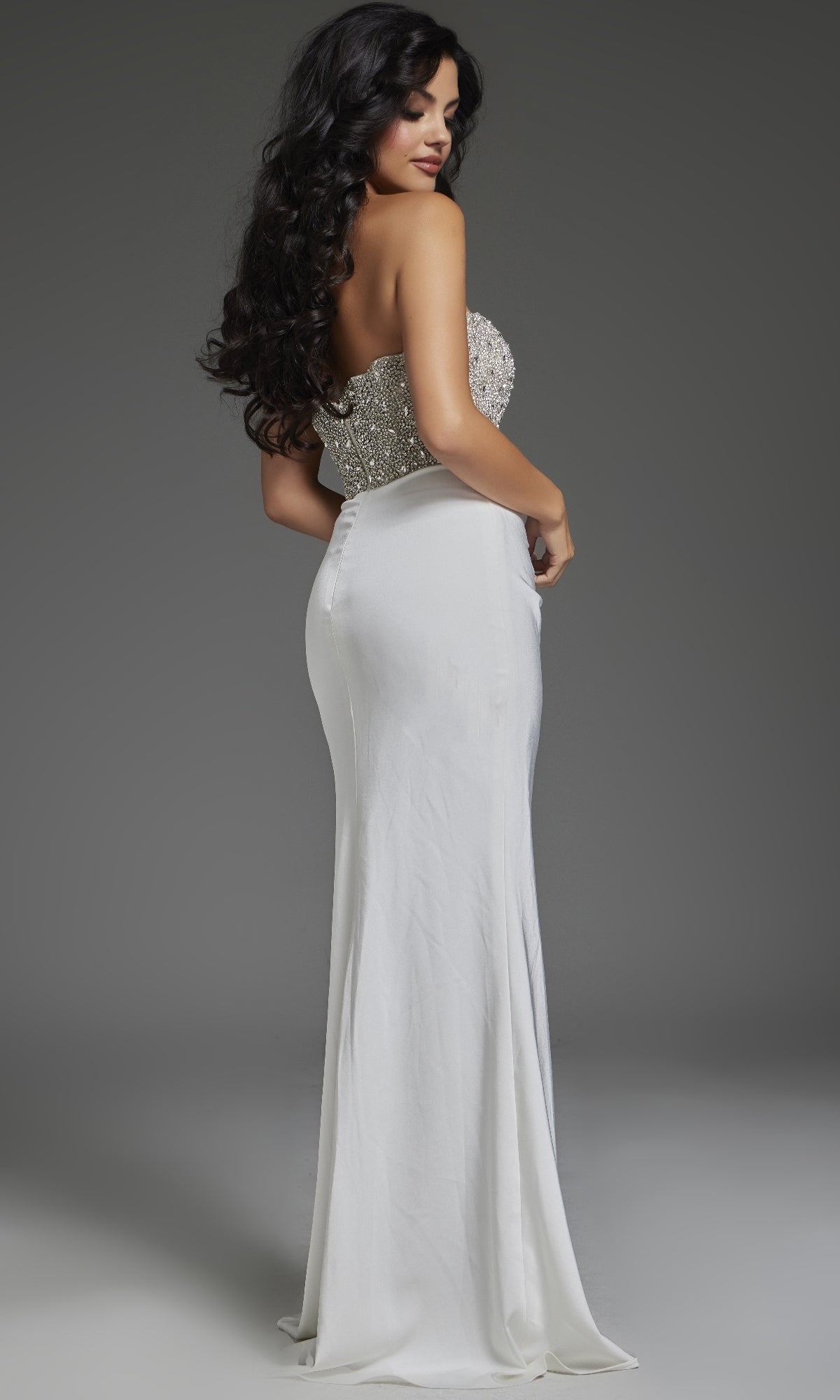 Model showcases the Jovani 42637 long prom dress, featuring a strapless design with a beaded bodice and high leg slit, standing slightly turned against a plain gray background.